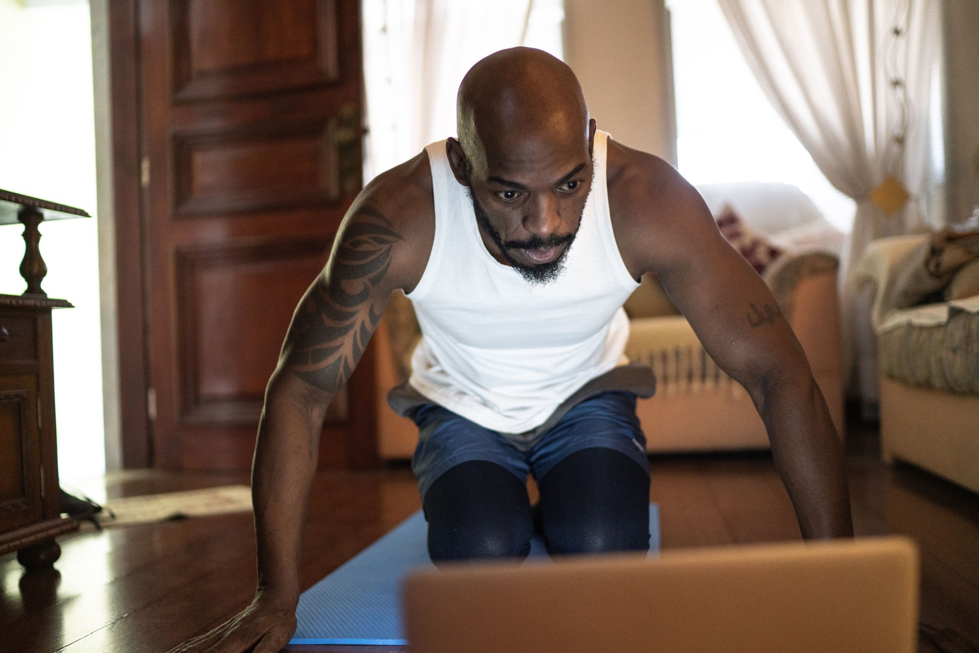 Man watching gym class on laptop and doing exercises at home